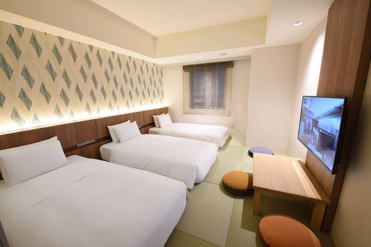 Ein Hotelzimmer mit drei Betten, einem Fernseher und einem kleinen Tisch.