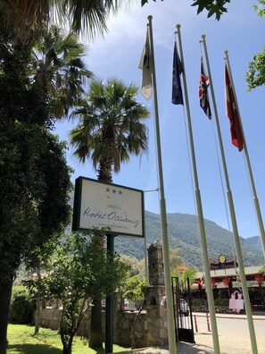 Un cartel de hotel con banderas, un muro de piedra y una montaña al fondo.