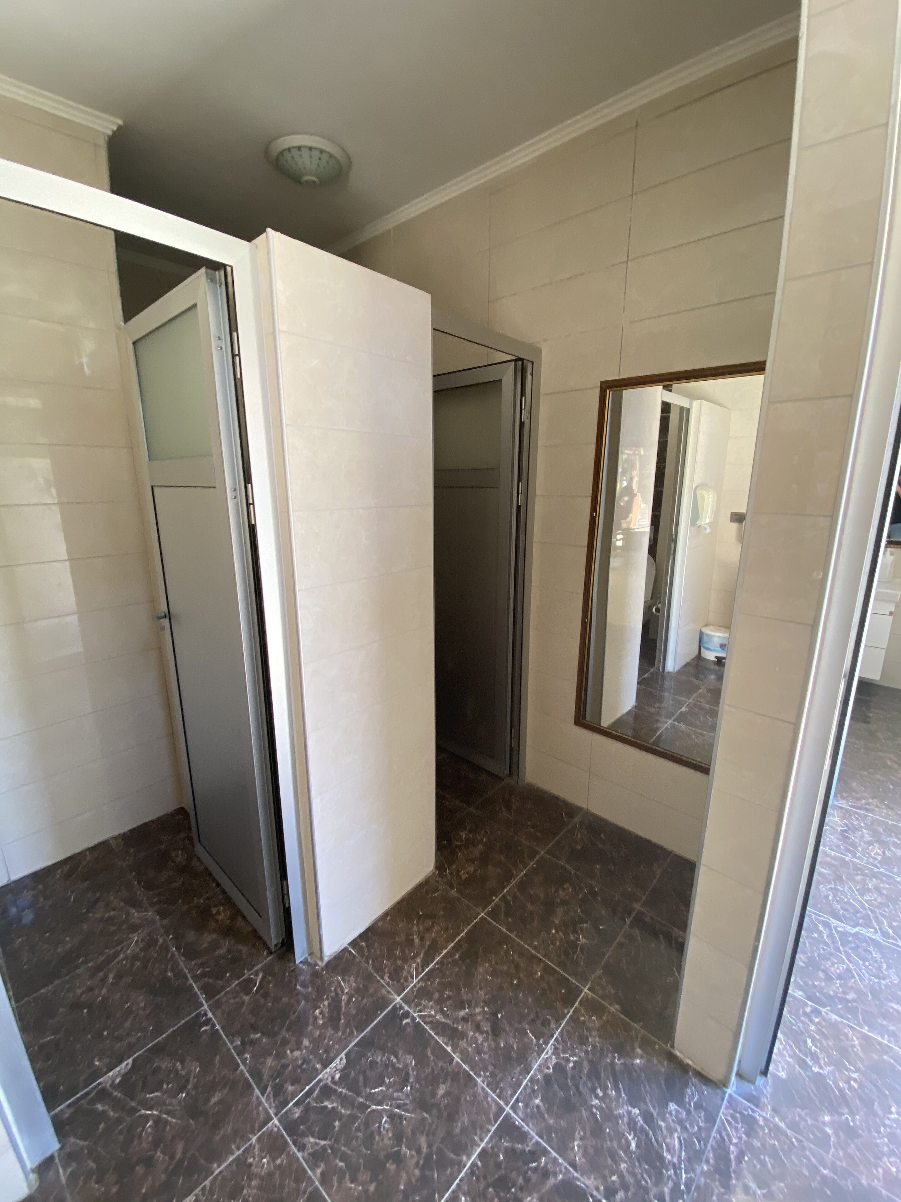 A bathroom with a tiled floor, a shower area, and a mirror.
