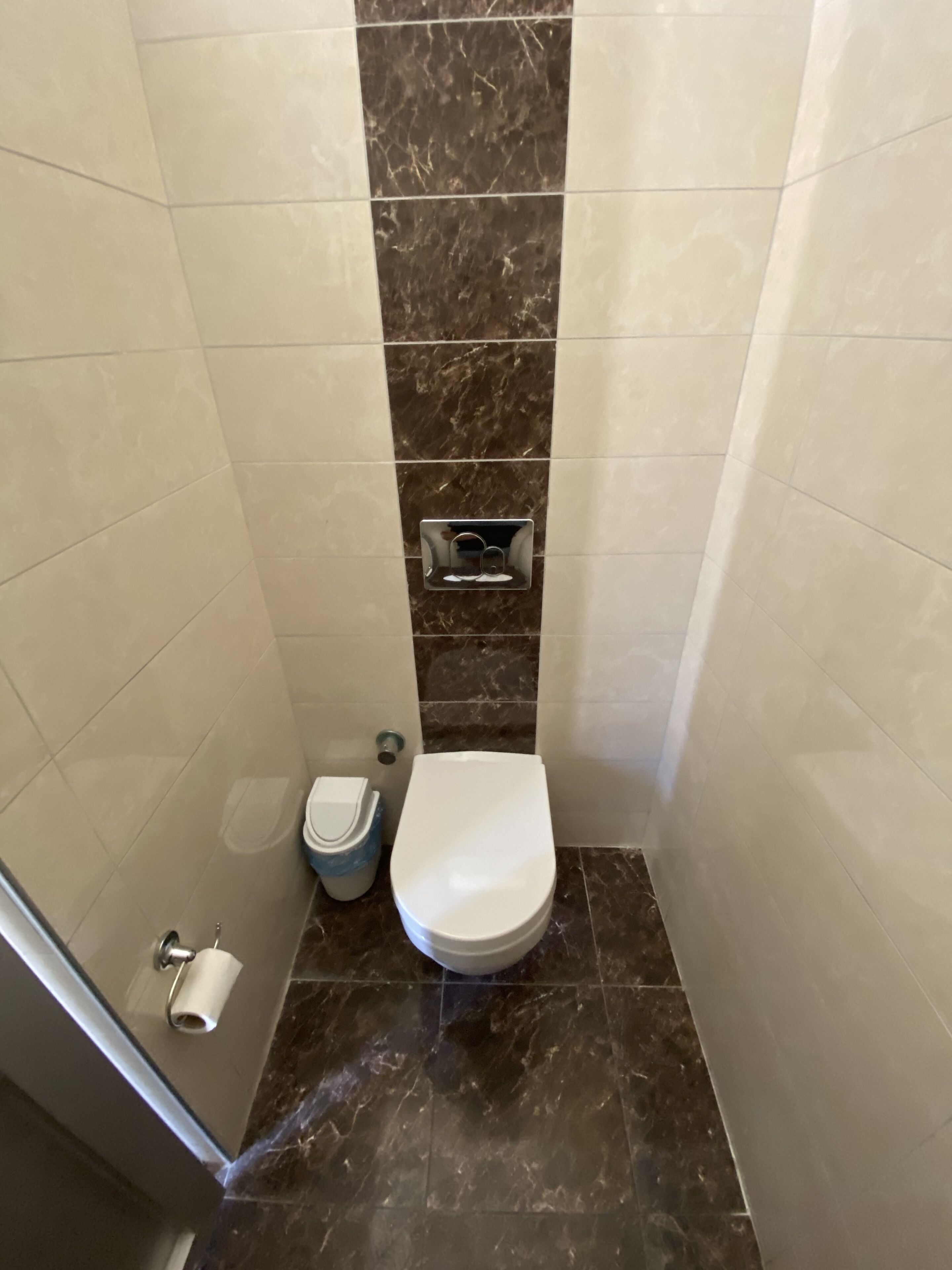Ein kleines Badezimmer mit Toilette, Mülleimer und Toilettenpapierhalter.