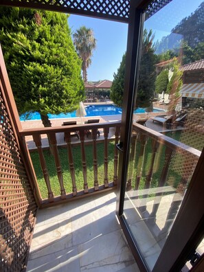 A balcony with a view of a swimming pool, a pergola, and a patio area with outdoor furniture.