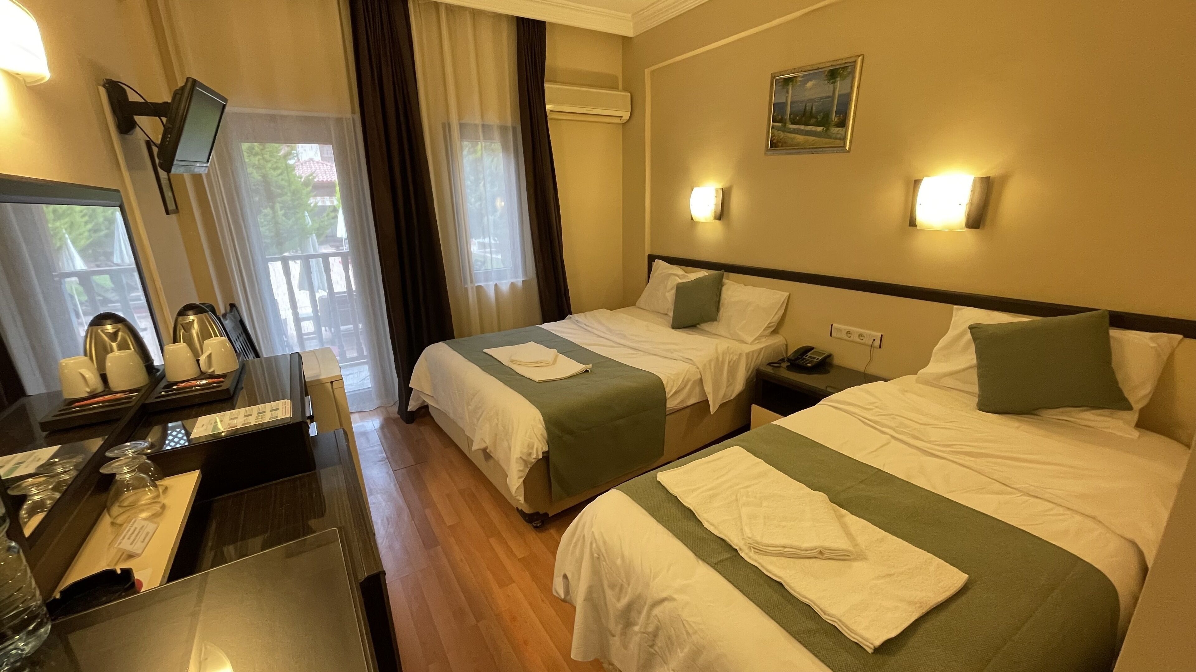 A hotel room with two beds, a desk with a coffee maker, a TV, and a painting on the wall.