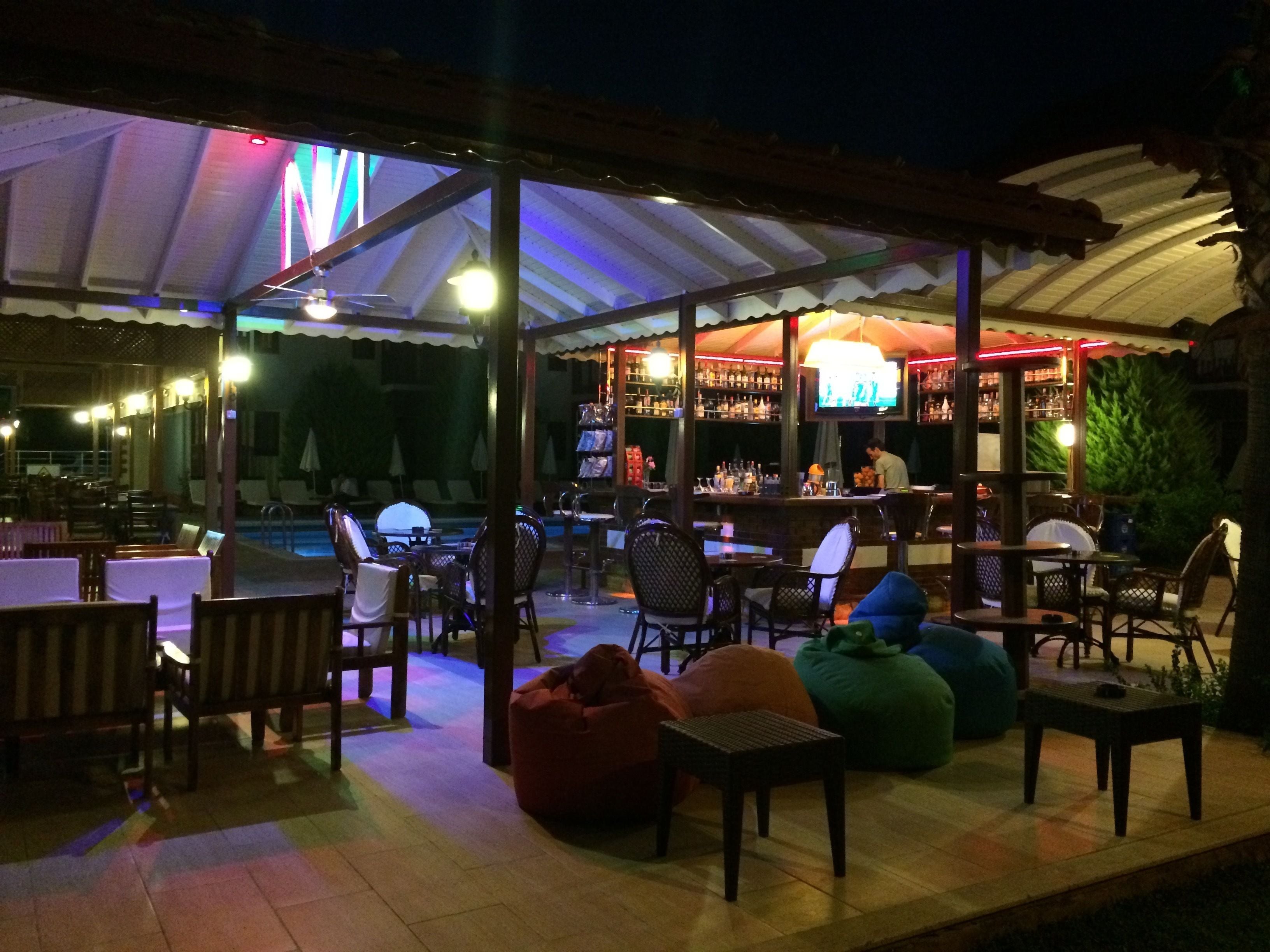 An outdoor bar area with tables and chairs, a pool, and a covered seating area.