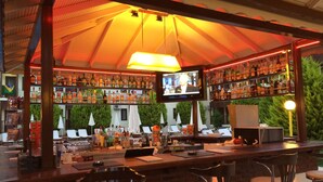 A bar area with a TV screen, multiple shelves of bottles, and bar stools. - Hotel Oludeniz (Fethiye)