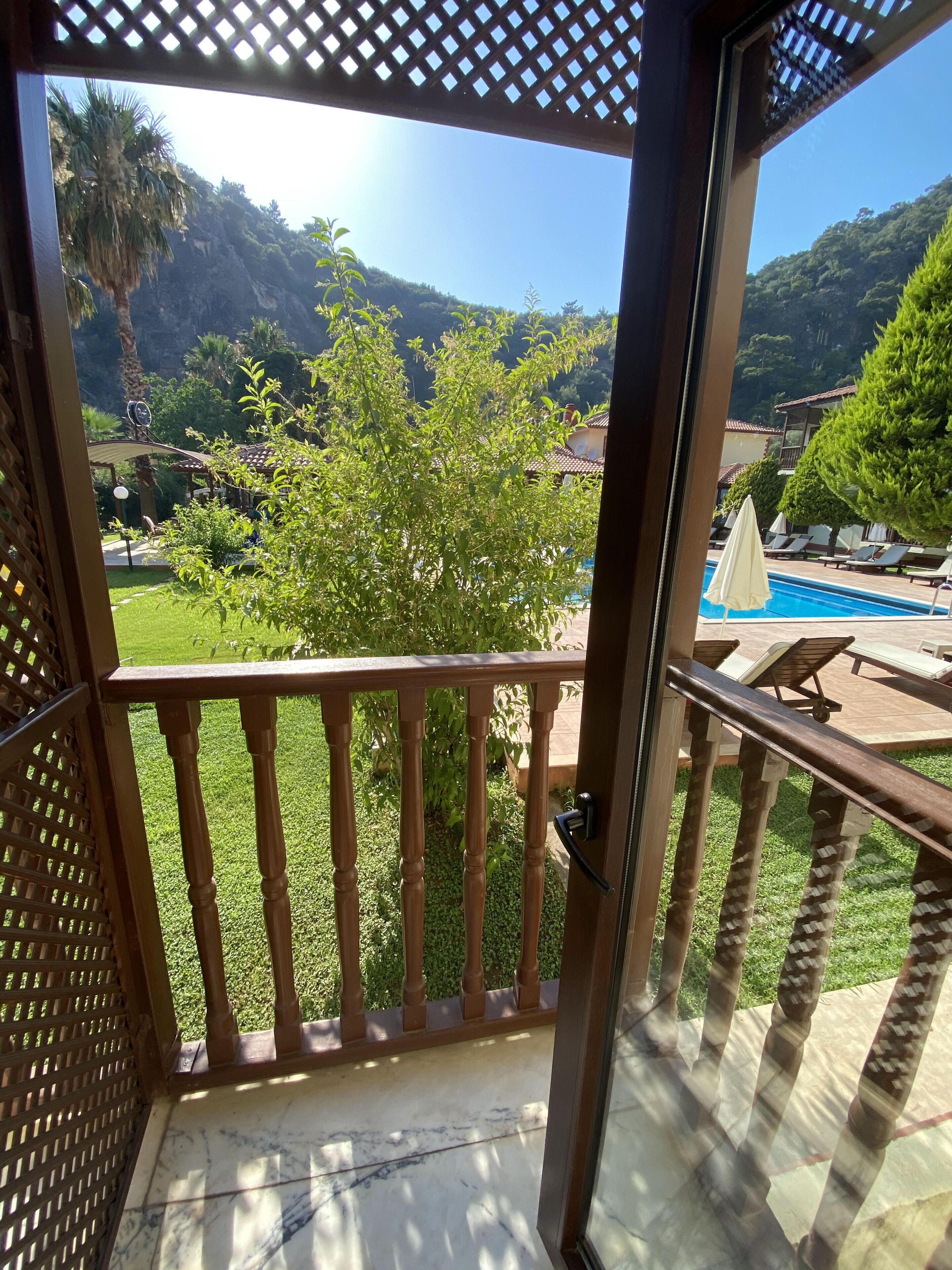 Ein Balkon mit Blick auf einen Swimmingpool, üppiges Grün und eine Berglandschaft.