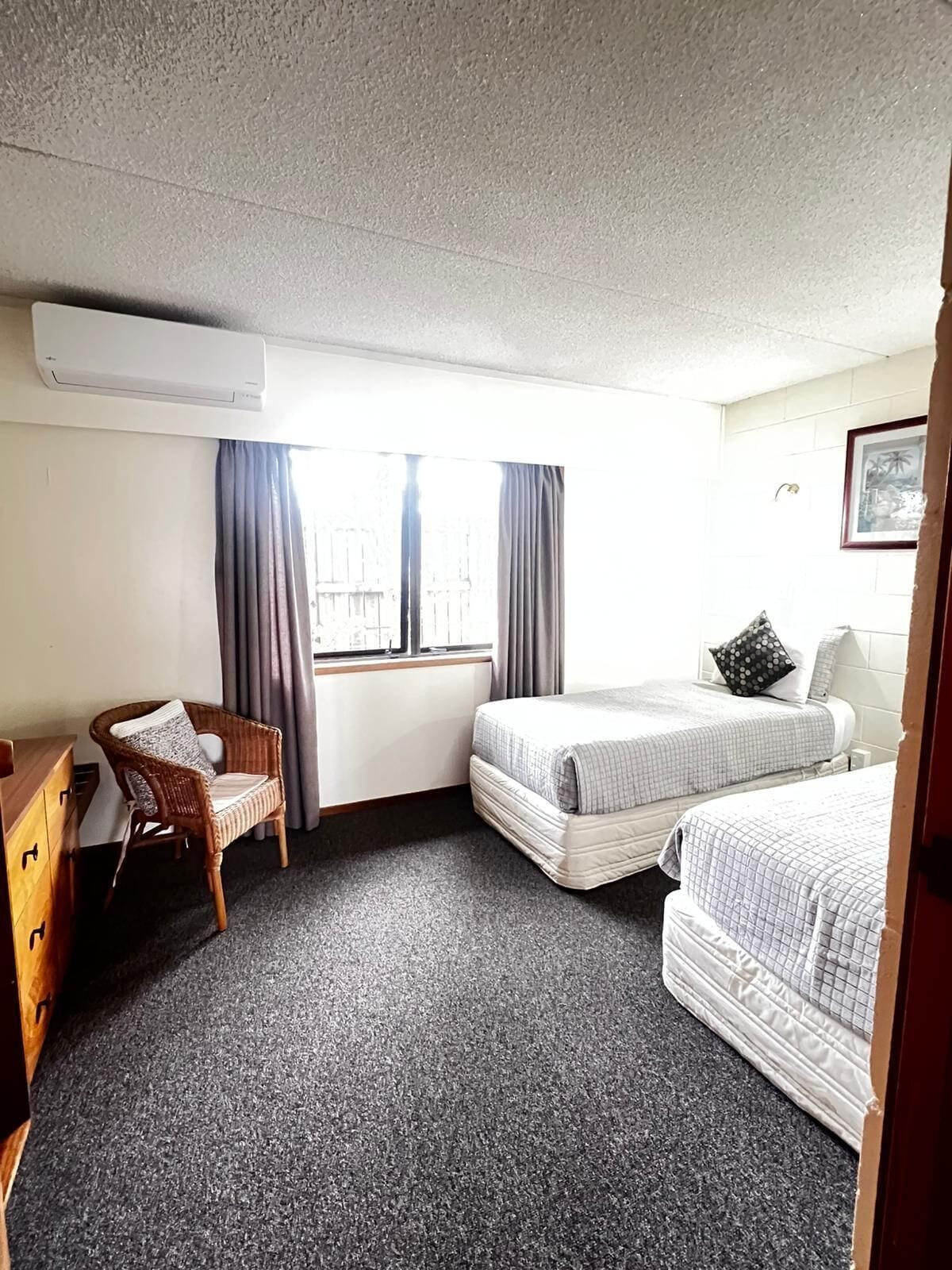 A hotel room with two beds, a chair, a dresser, and a window with curtains.