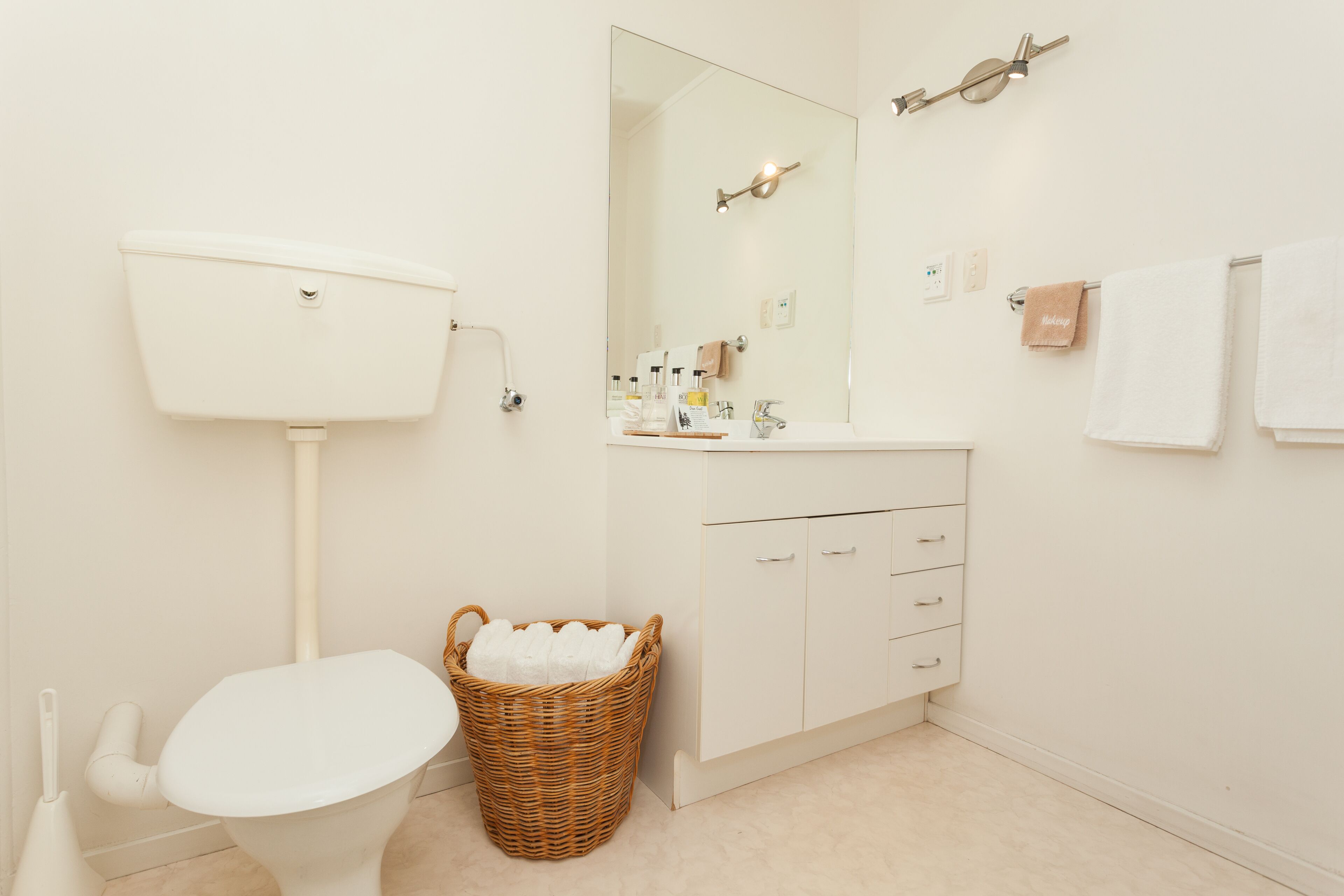 A bathroom with a toilet, a sink, a mirror, and a wicker basket.
