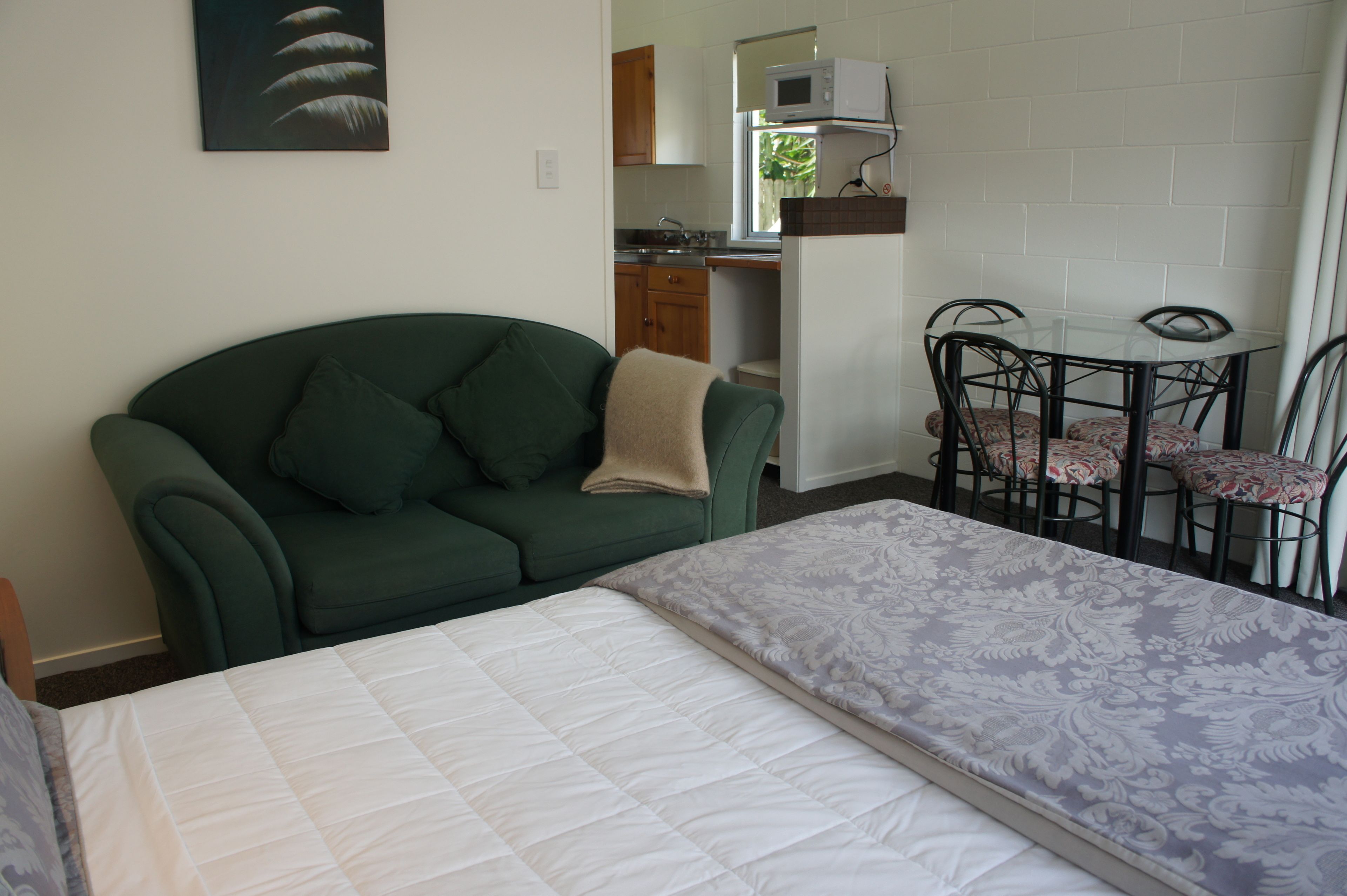 Una habitación con una cama, un sofá verde, una mesa de comedor con sillas, un microondas y una ventana con cortinas.