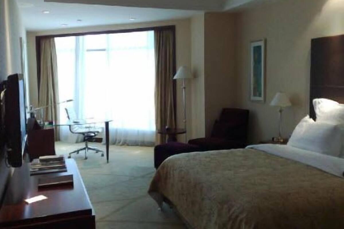 A hotel room with a large bed, a desk with a chair, a TV, and a window with curtains.