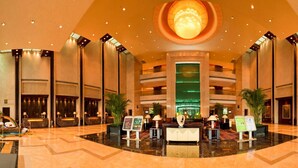 Eine großzügige Lobby mit einem zentralen Atrium, mehreren Rezeptionstheken und einer großen, beleuchteten Globus-Skulptur.