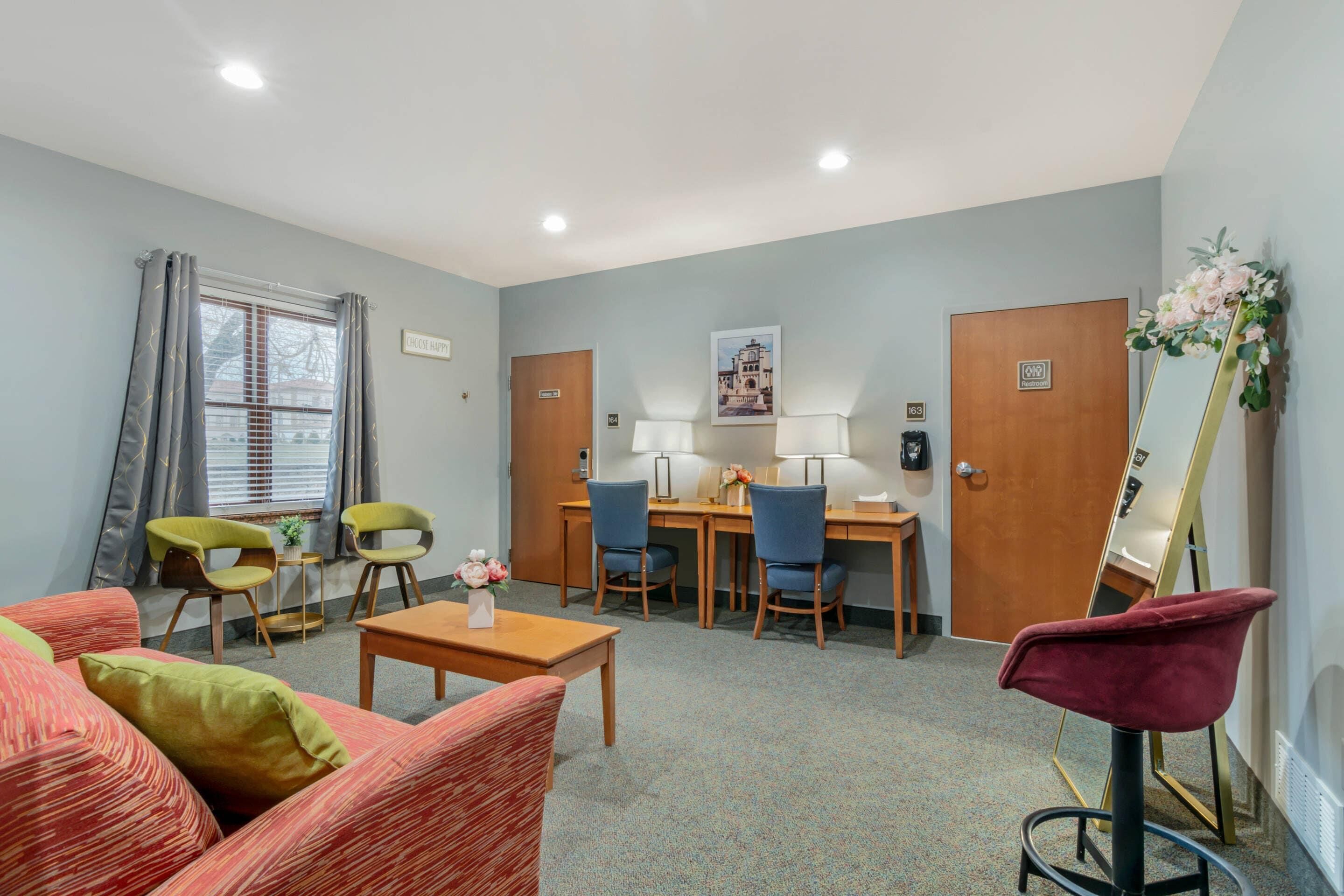 A hotel room with a seating area, a desk, and a mirror.