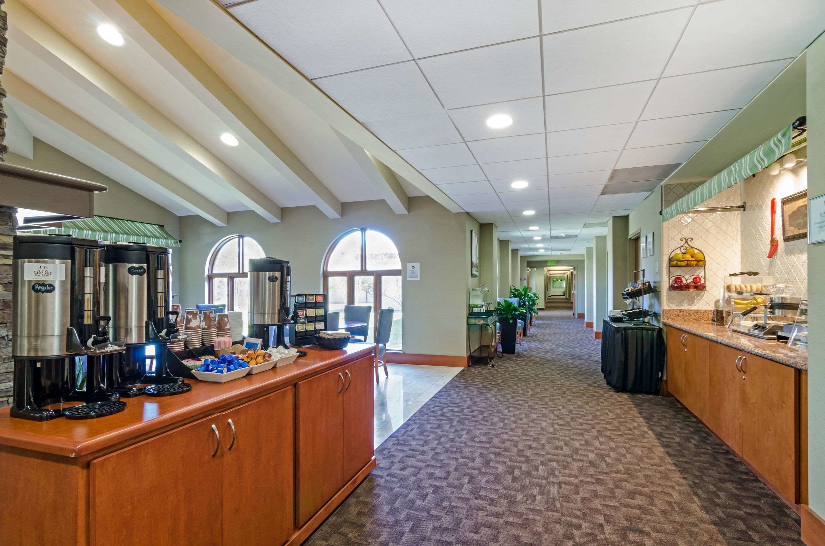 A hotel lobby with a coffee station, seating area, and a view of the hallway.