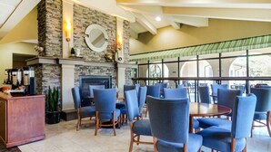 A spacious indoor area with a stone fireplace, blue upholstered chairs, and a large window overlooking a green outdoor area.