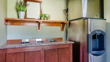 Una cocina con refrigerador de acero inoxidable, encimera de granito y repisa de madera con plantas en macetas.