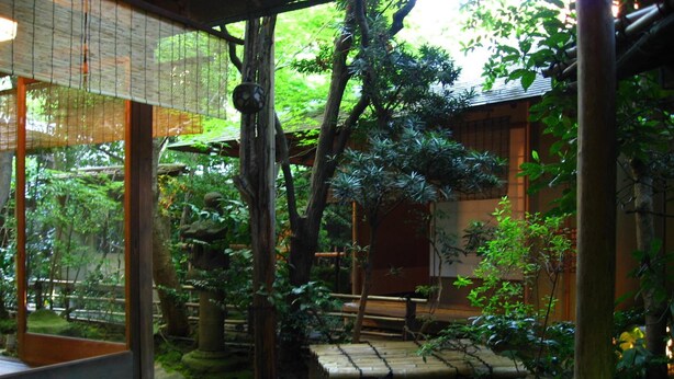 Um jardim japonês tradicional com caminhos de pedra, estruturas de madeira e vegetação exuberante.