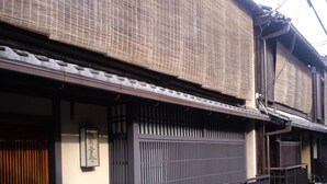 Um edifício japonês tradicional com telhado de telhas, portão de entrada de madeira e cerca de metal preto.