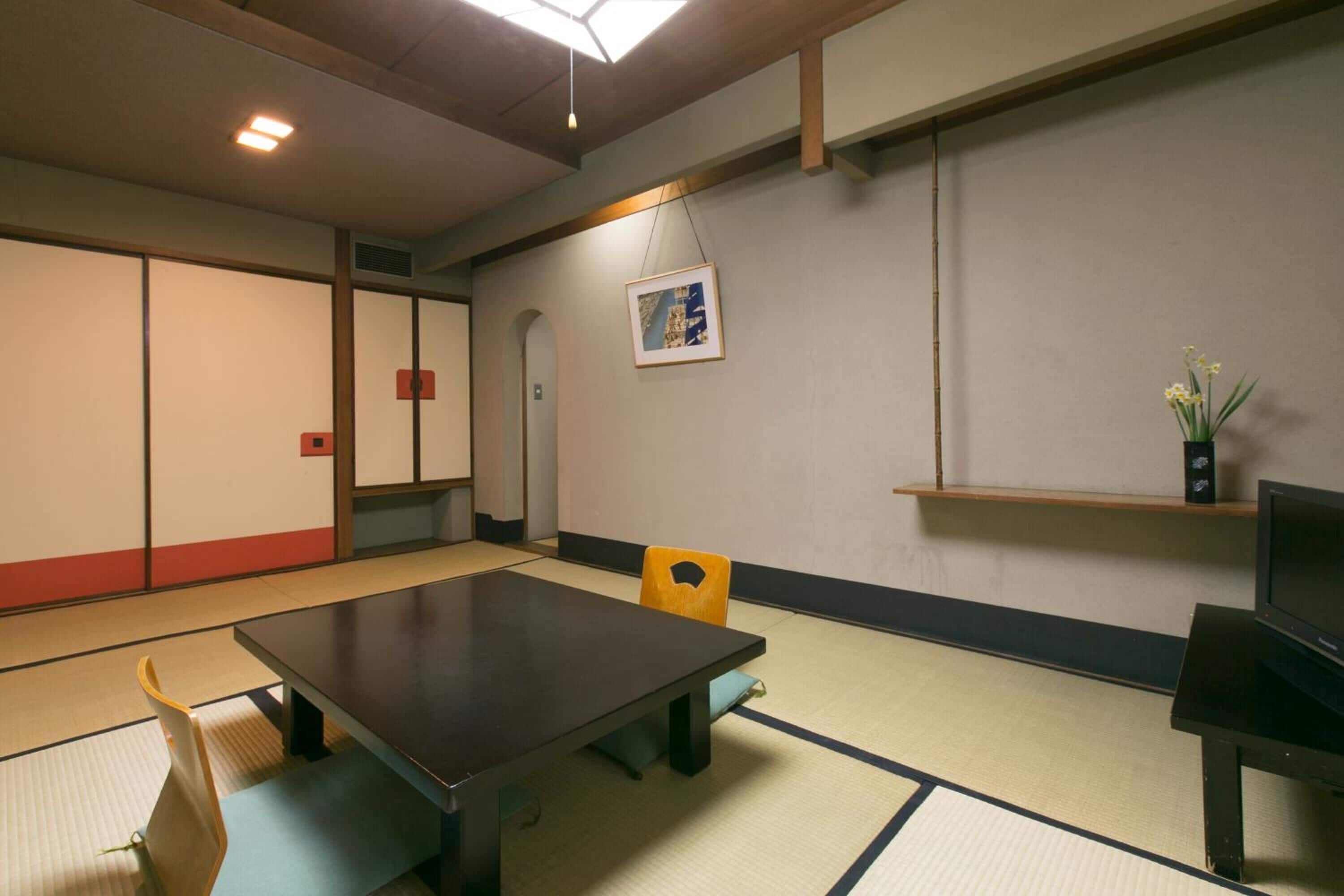 A traditional Japanese room with tatami flooring, a low table, a yellow chair, and a small shelf with a vase.