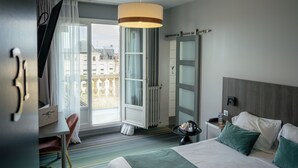 A hotel room with a bed, a desk, a chair, a window with curtains, a radiator, and a view of buildings outside. - Hotel Central (Poitiers)