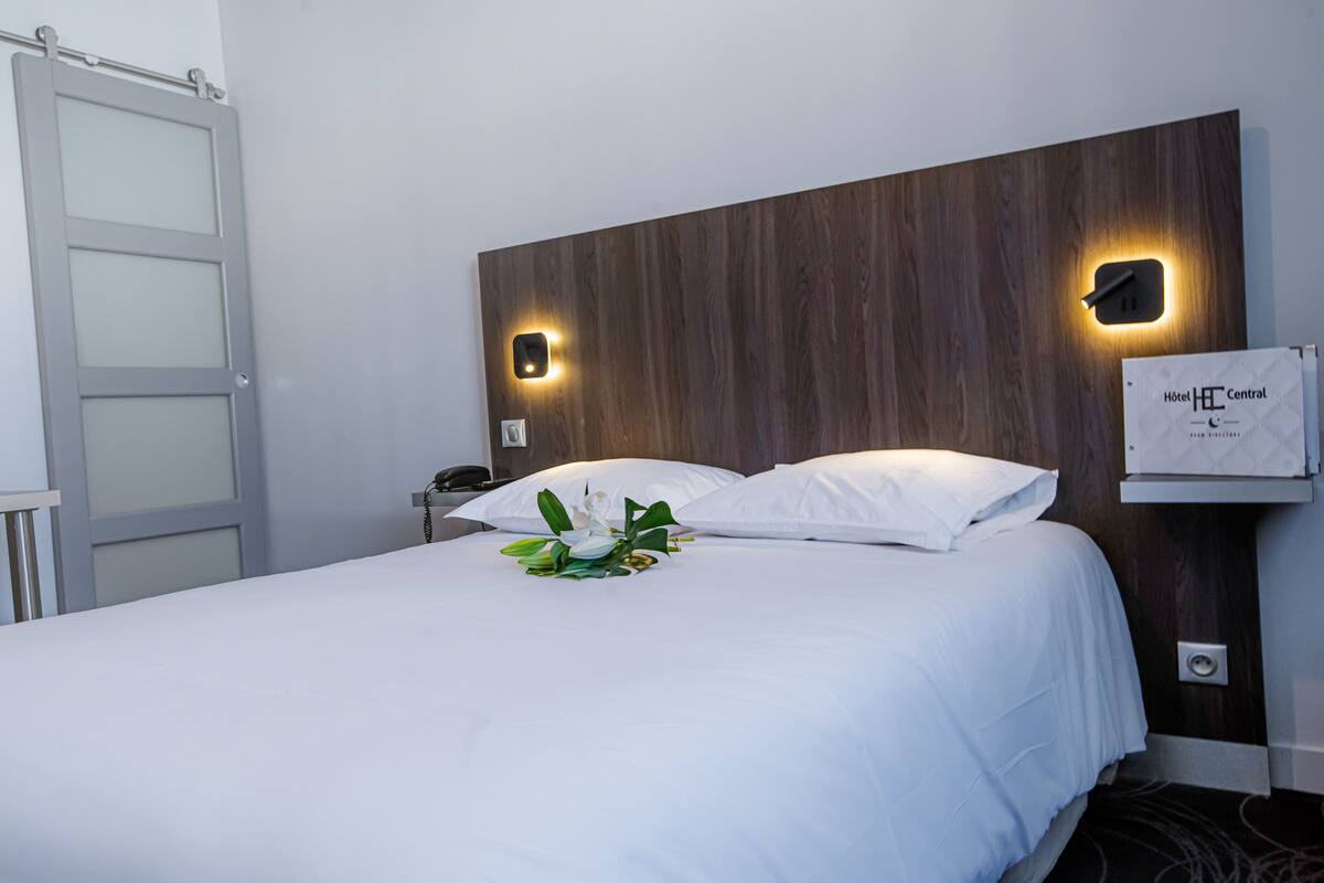A neatly made bed with white linens, a wooden headboard, and two wall-mounted light fixtures.
