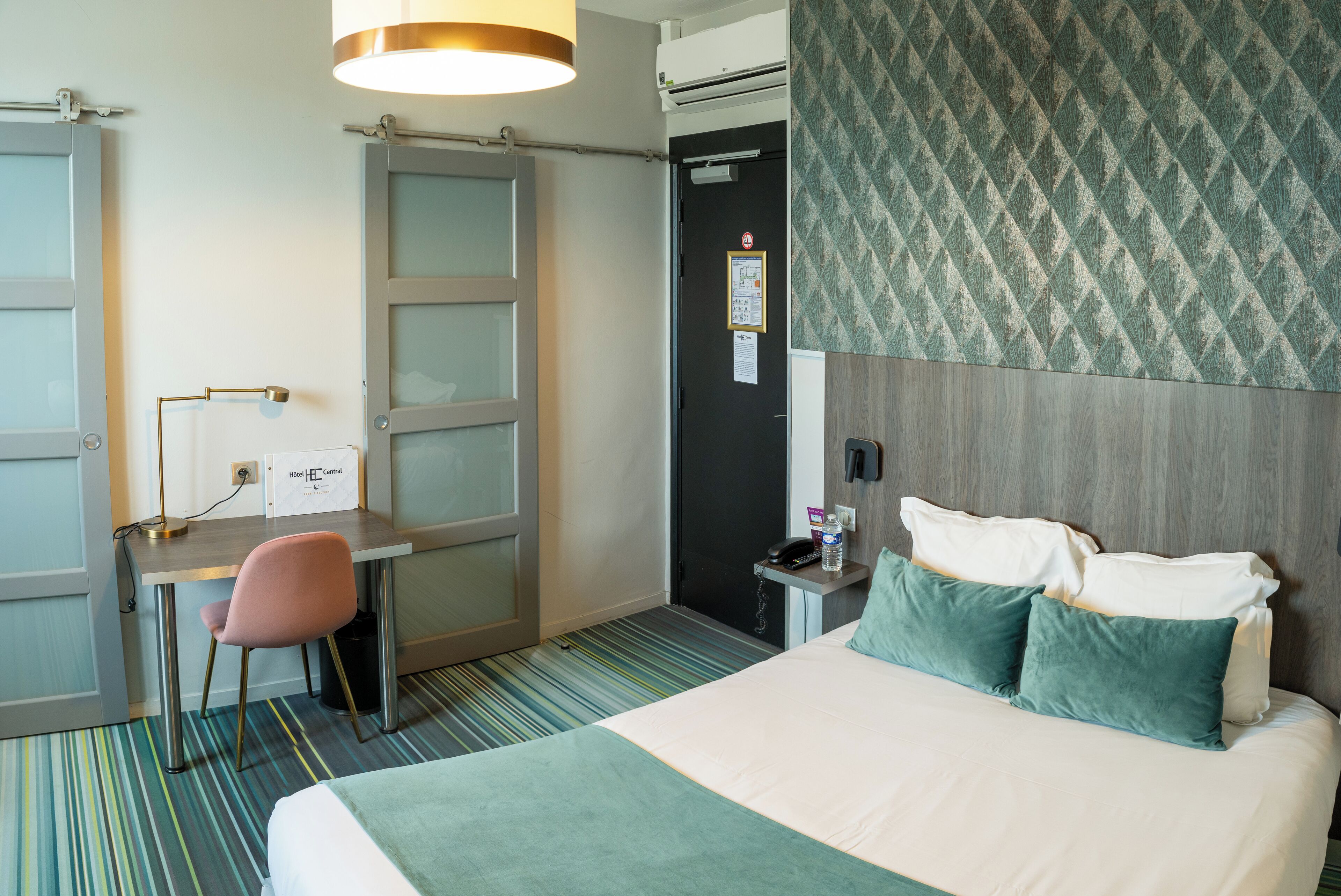 Une chambre d’hôtel comprenant un lit, un bureau, une chaise et une table de chevet avec une lampe.