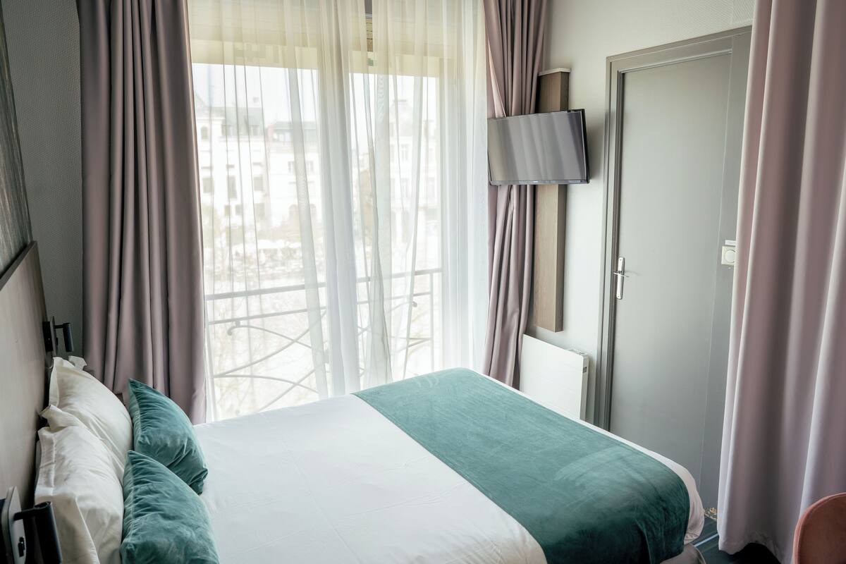 A hotel room with a bed, a TV mounted on the wall, and a door.