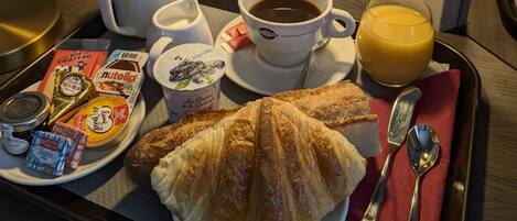 Un plateau de petit-déjeuner avec des croissants, du café, du jus de fruits, ainsi qu’une variété de viennoiseries et de confitures.