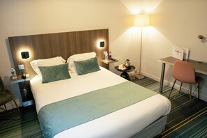 A hotel room with a large bed, bedside tables, a desk, a chair, and a lamp. - Hotel Central (Poitiers)