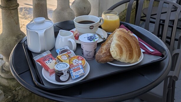 A balcony table with breakfast items, including croissants, coffee, and juice, overlooking a historic building with ornate architecture. - Hotel Central (Poitiers)