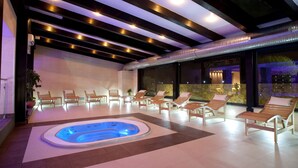 Un espace piscine intérieur moderne, doté d’un jacuzzi, de chaises longues et d’un plafond pourvu d’un système d’éclairage linéaire.