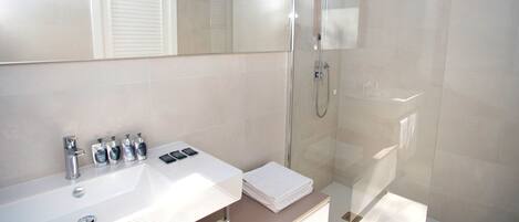 Un baño moderno con un lavabo blanco, varios dispensadores de jabón, una cabina de ducha de vidrio y un espejo sobre el lavabo.