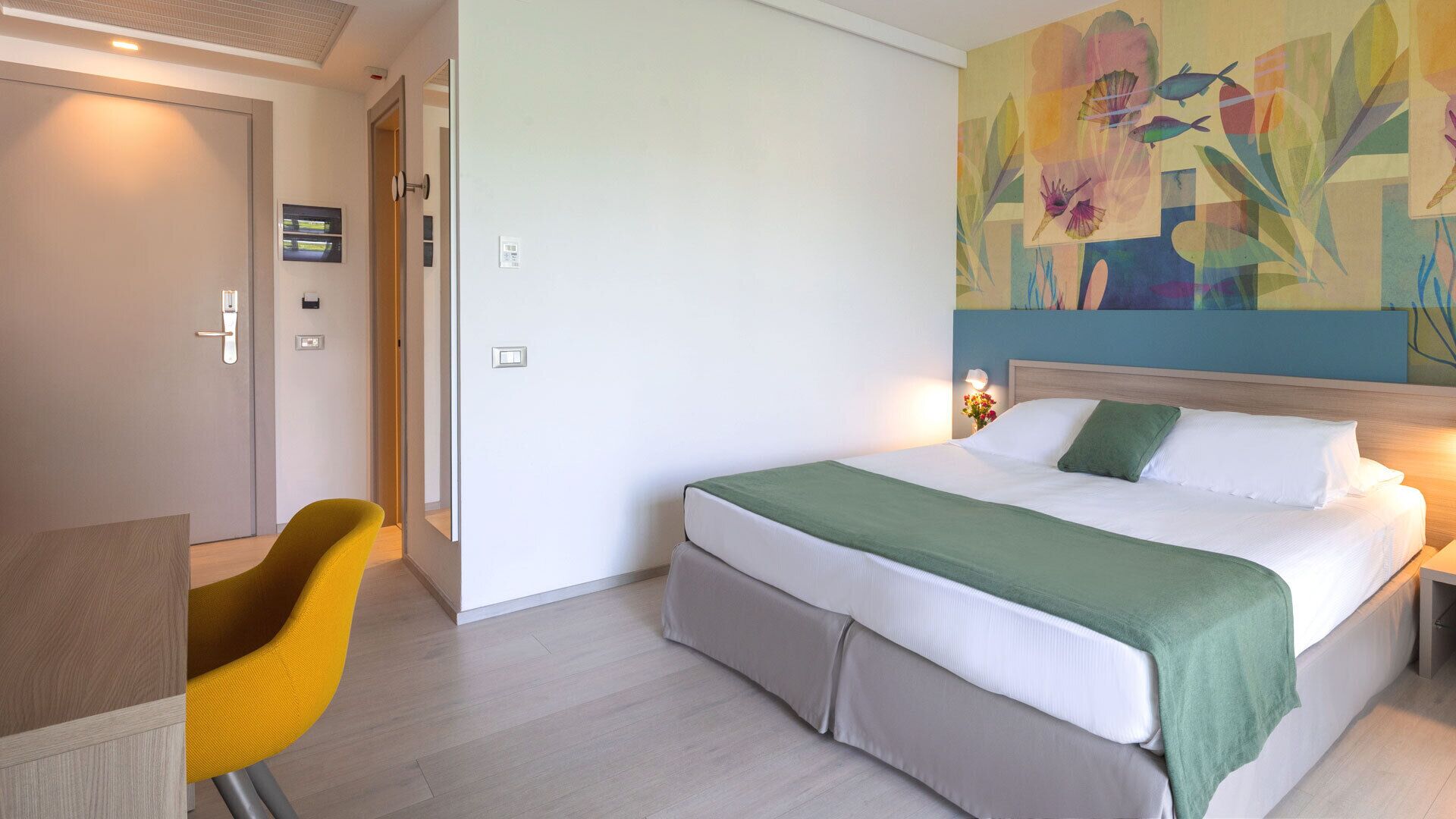 A hotel room with a bed, a desk, a chair, and a colorful abstract painting on the wall.