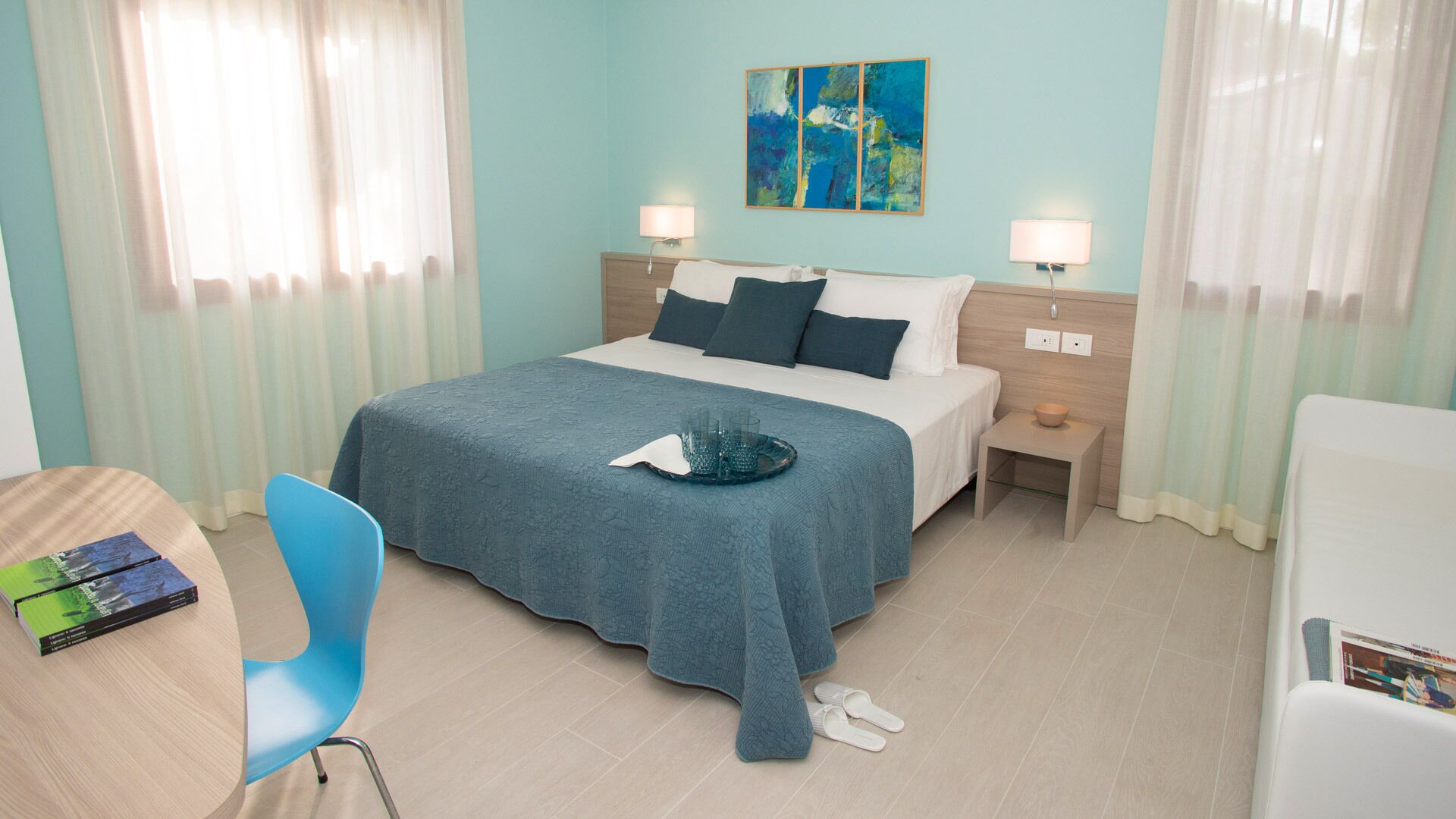 Een hotelkamer met een bed, nachtkastjes, een bureau, een stoel en een schilderij aan de muur.