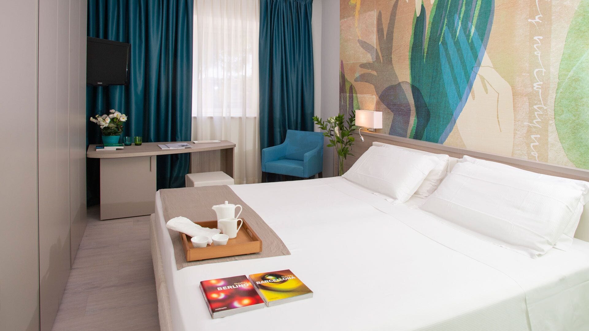 A hotel room with a bed, a desk, a chair, and a painting on the wall.