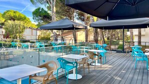 An outdoor patio with glass tables and chairs, umbrellas, and a wooden deck.