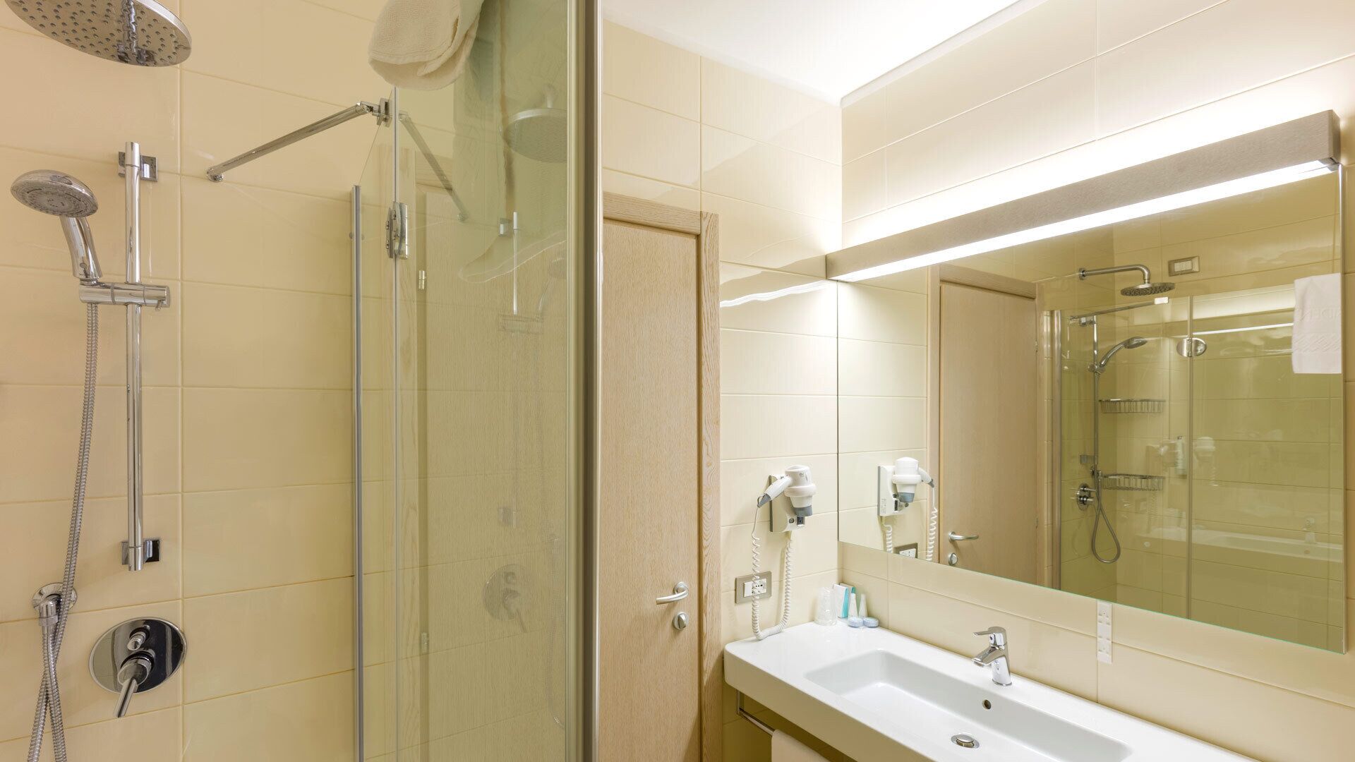 A modern bathroom with a glass-enclosed shower, a sink with a mirror, and a towel hanging on the wall.