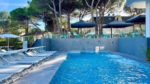 A swimming pool with lounge chairs and umbrellas, surrounded by trees and a building with a balcony.