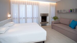 A hotel room with a bed, a sofa, a fireplace, and a bookshelf.