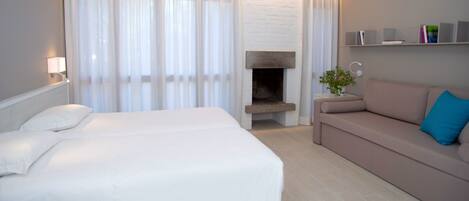 A hotel room with a bed, a sofa, a fireplace, and a bookshelf.
