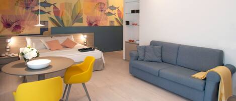 Una habitación de hotel moderna con cama, sofá, mesa de comedor con sillas y un mural decorativo.