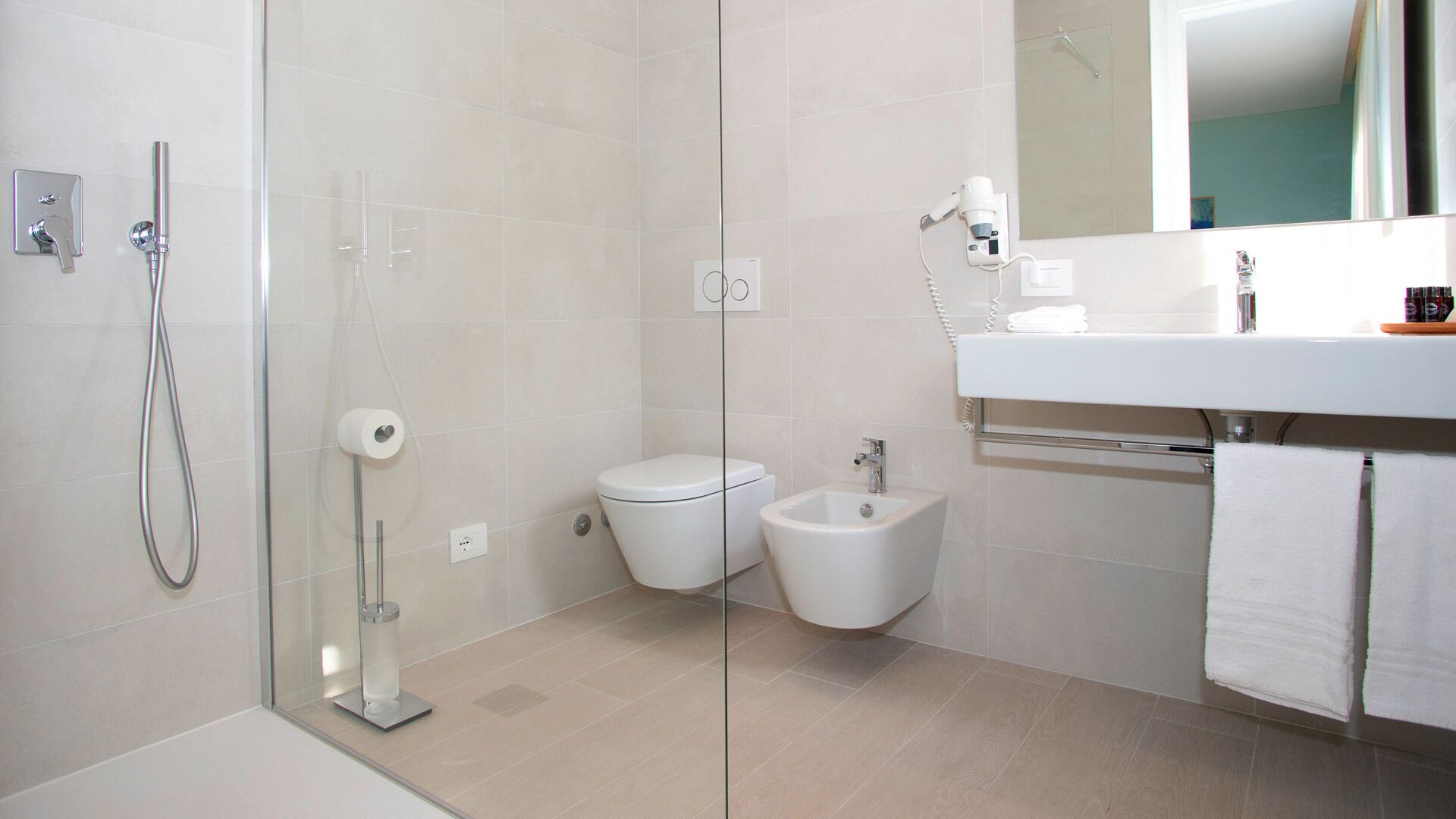 A modern bathroom with a glass shower enclosure, a toilet, bidet, and a sink with a mirror above.