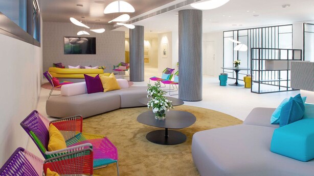 A modern living room with a sectional sofa, colorful chairs, a coffee table, and a large window.