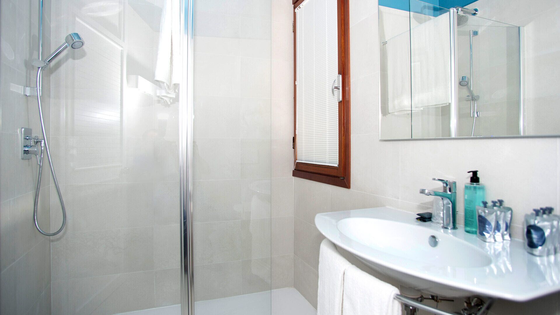 A modern bathroom with a glass shower enclosure, a white sink with toiletries, and a mirror above the sink.