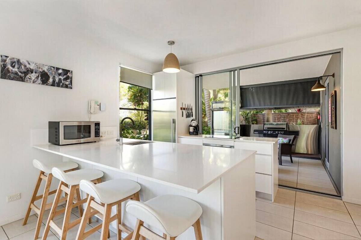 Una cocina moderna con una isla central, taburetes de bar y vistas al área exterior.