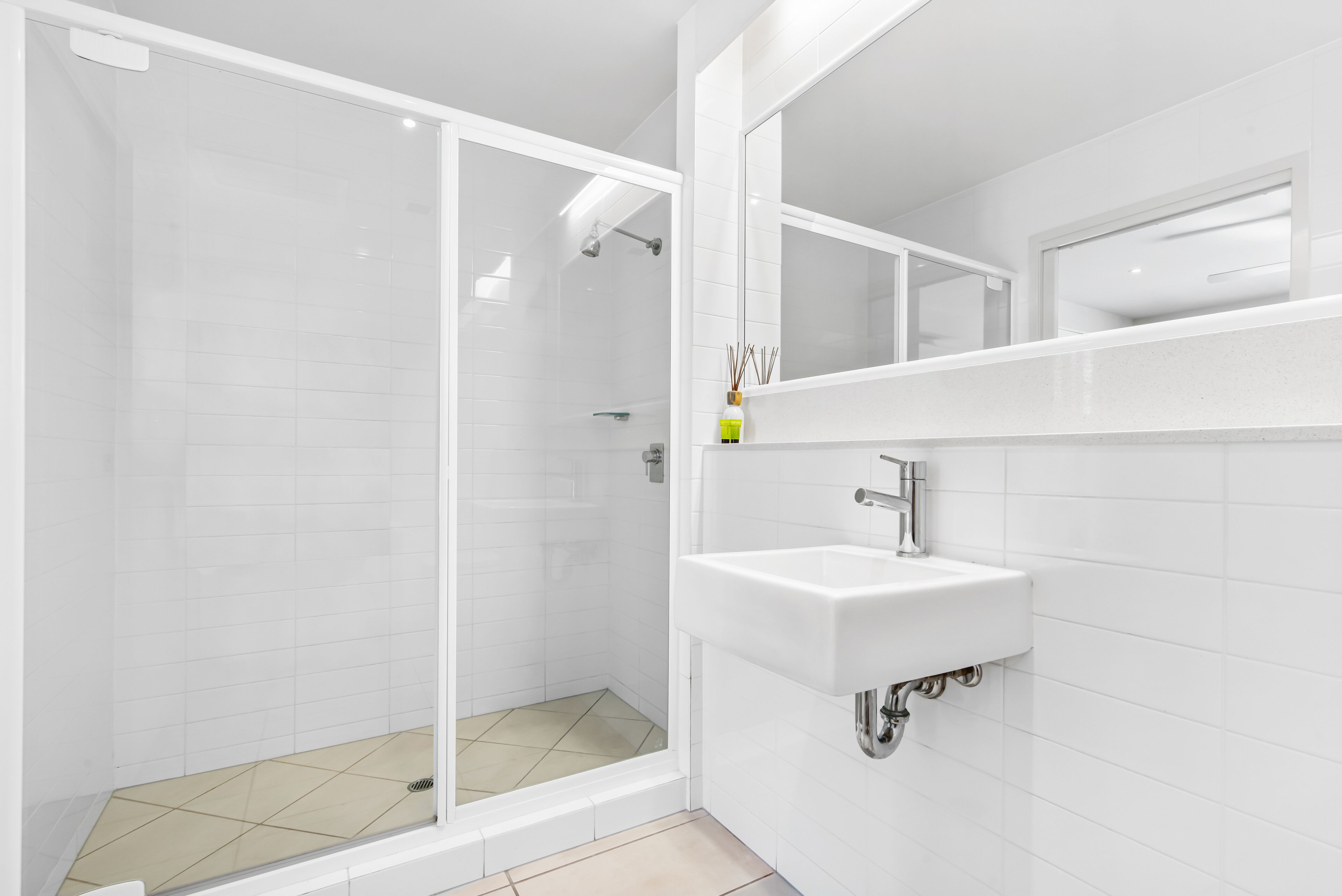 Une salle de bain moderne avec une douche à parois de verre, un lavabo blanc et un grand miroir au-dessus du lavabo.