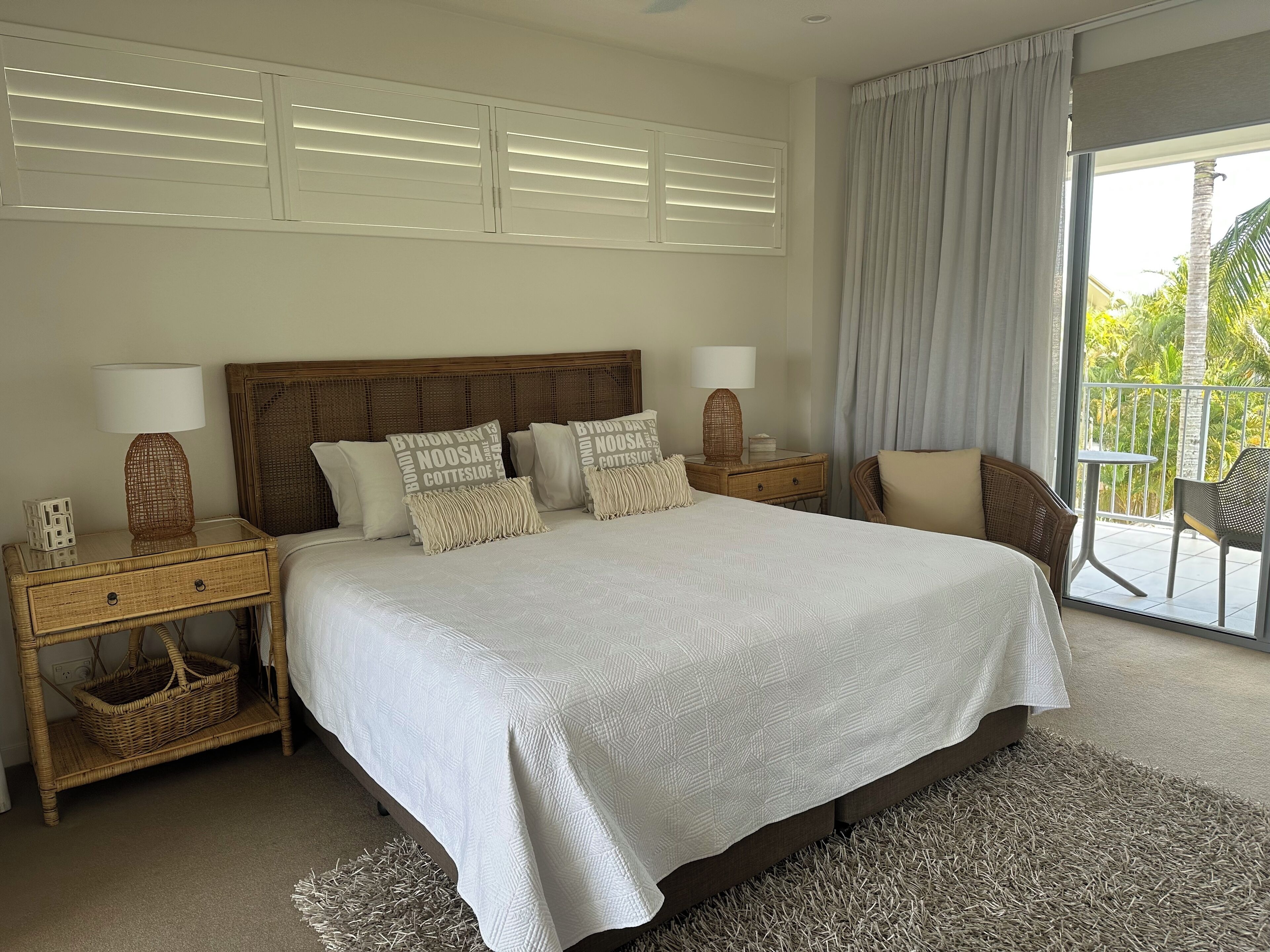 Une chambre à coucher avec un grand lit, deux tables de chevet, une tête de lit et une vue sur l’extérieur.