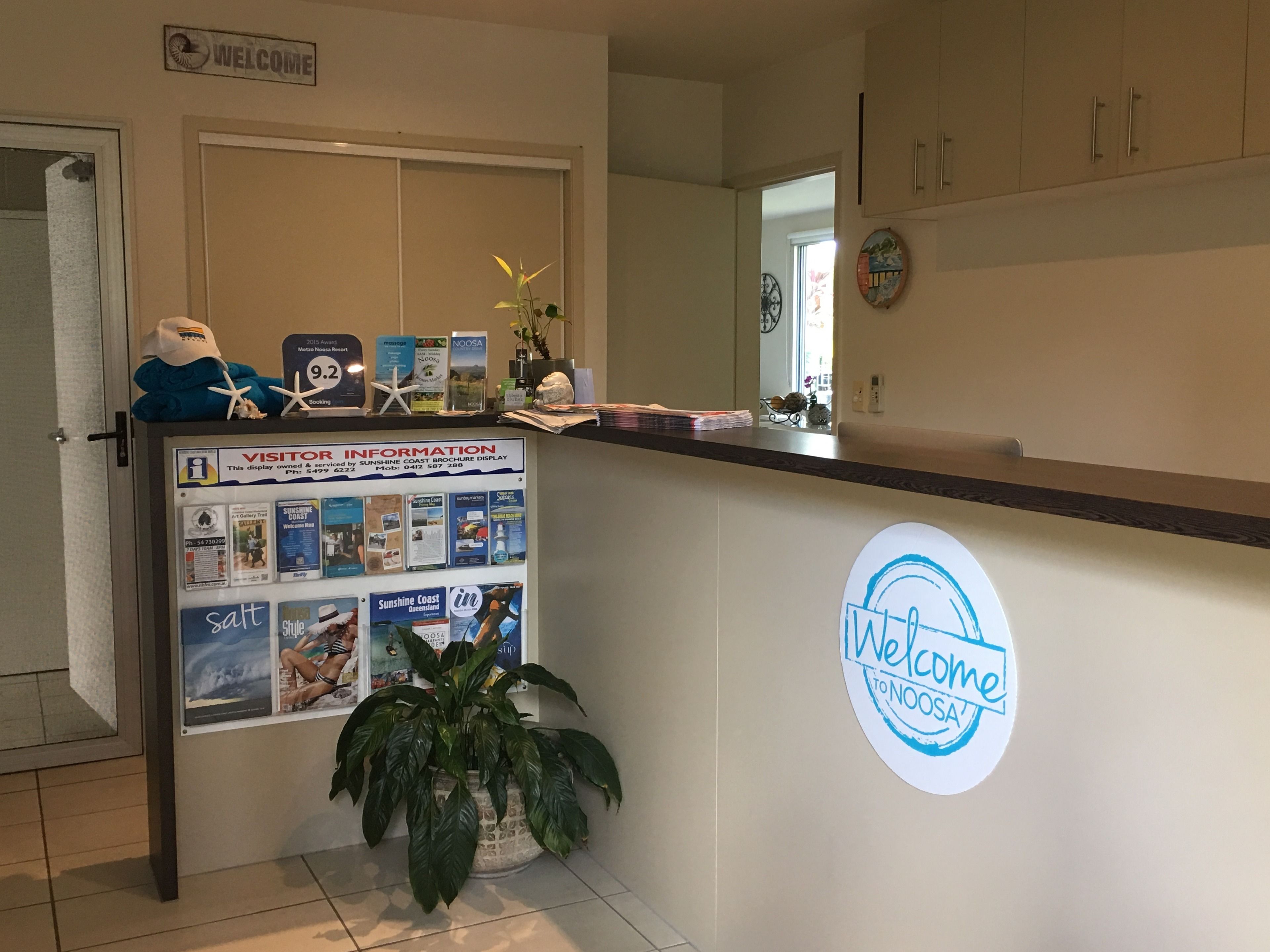 Zona de recepción con un letrero de bienvenida, un tablón de anuncios con información para visitantes y una planta.