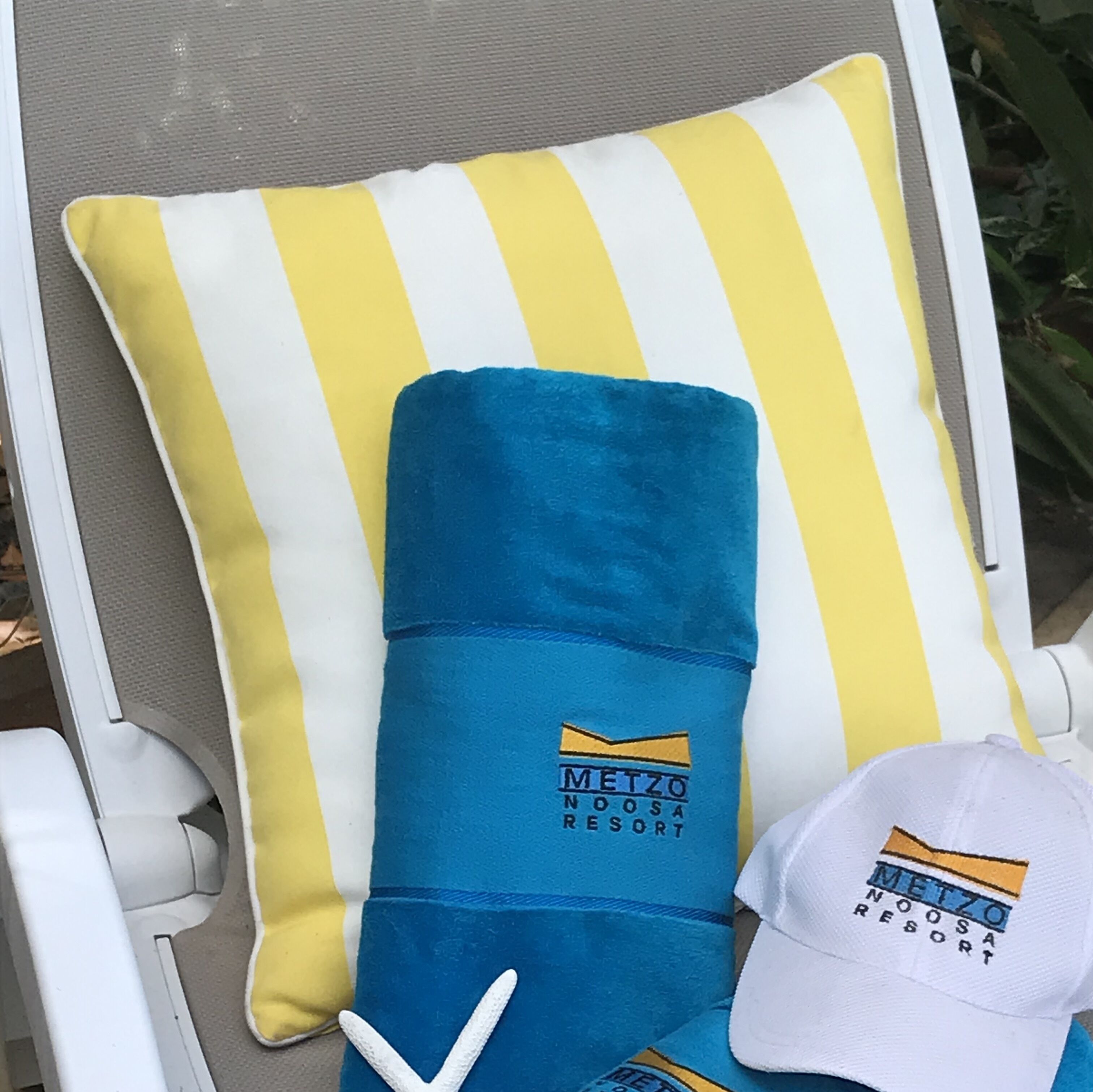 A lounge chair with a yellow and white striped pillow and a blue pillow with a logo.