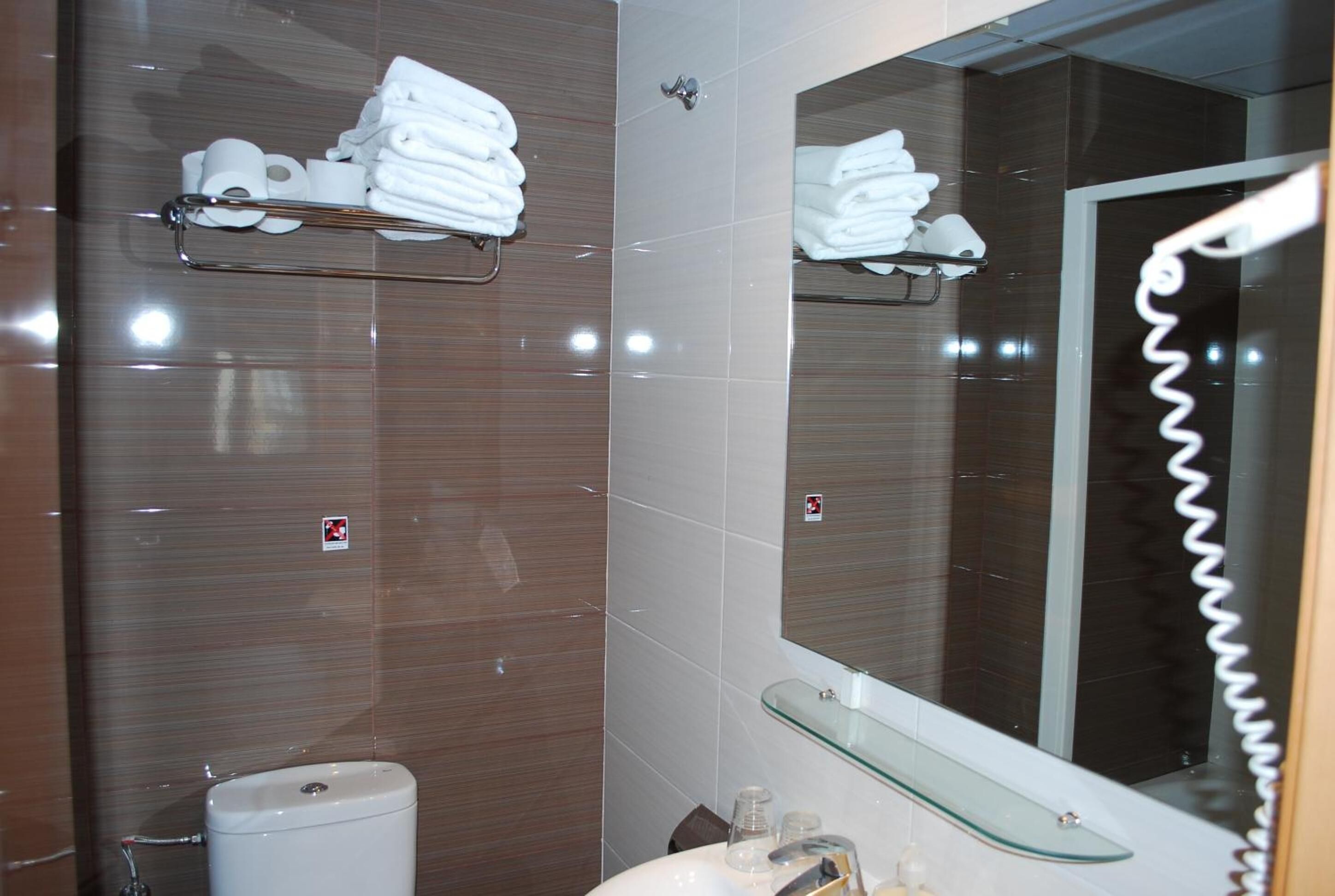 Une salle de bain équipée de toilettes, d’un lavabo et d’étagères en verre où sont rangées les serviettes.