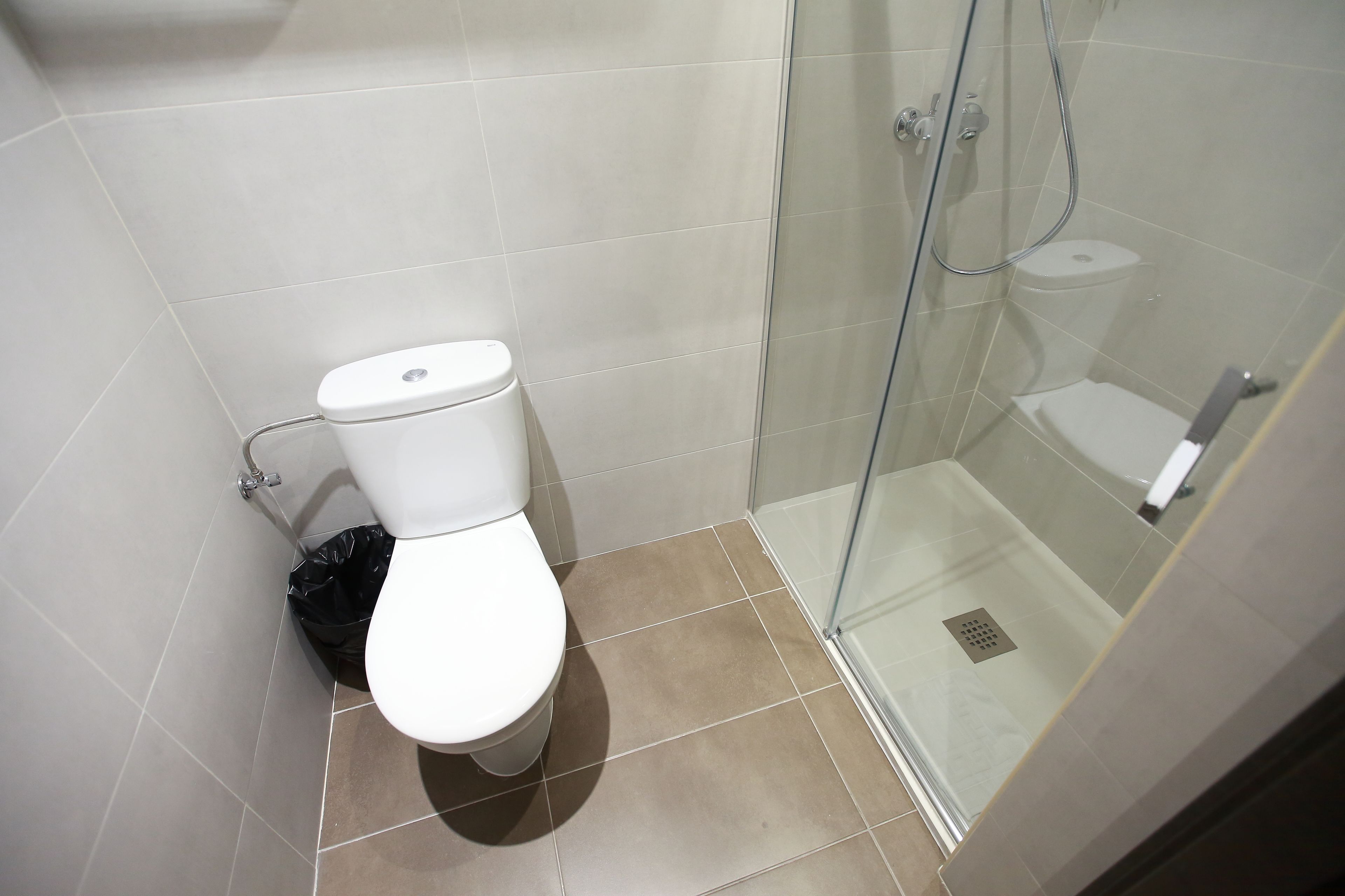 A bathroom with a toilet, a glass-enclosed shower, and a black trash bin.