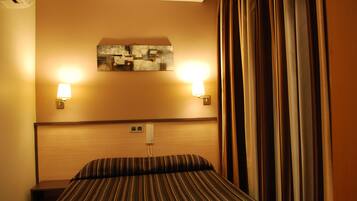 Habitación de hotel con cama, dos lámparas fijadas a la pared, un cuadro sobre la cama y un teléfono en la pared.